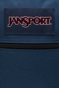 Blå Jansport ryggsekk med teksturert overflate, med et fremtredende broderte logo og svarte glidelåsdetaljer.