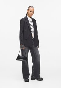 Fekete zakó egy fehér grafikus póló fölött, szürke széles szárú farmernadrág és egy kisebb fekete lakk kézi táska. Fekete platform cipők teszik teljessé a megjelenést.