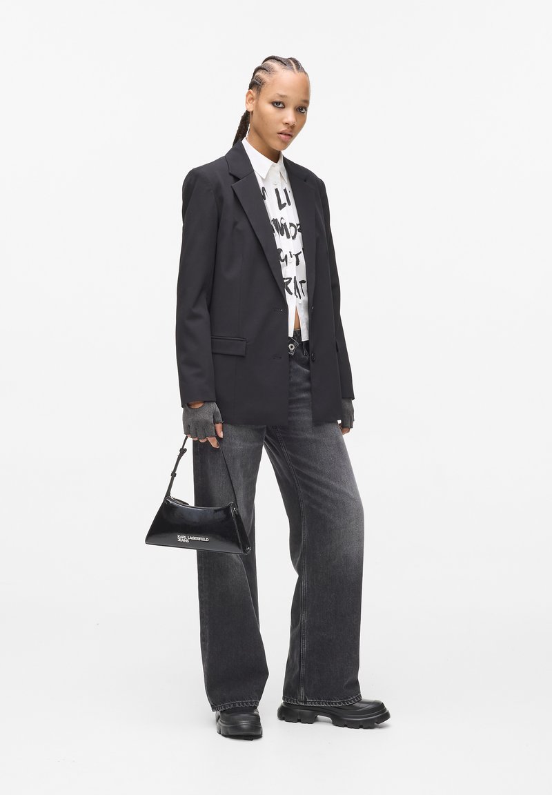 Fekete zakó egy fehér grafikus póló fölött, szürke széles szárú farmernadrág és egy kisebb fekete lakk kézi táska. Fekete platform cipők teszik teljessé a megjelenést.