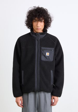 Veste en polaire noire avec poche poitrine zippée et poches latérales, présentant des panneaux texturés contrastés et un col montant.