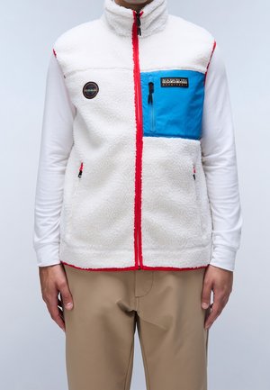 Mann trägt eine weiße Fleeceweste mit rotem Reißverschluss, blauer Brusttasche und rundem Logo, darüber ein weißes Langarmshirt und beige Hose.