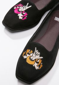 Ballerine in suede nero con punta quadrata. Presentano ricami a mano multicolore: rosa e bianco su una scarpa, arancione e bianco sull'altra.