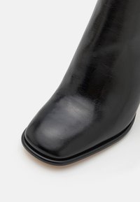 Czarne skórzane botki za kostkę o kwadratowym nosku, gładkiej texture i subtelnym połysku, z zaokrągloną cholewką i minimalistycznym wzornictwem.