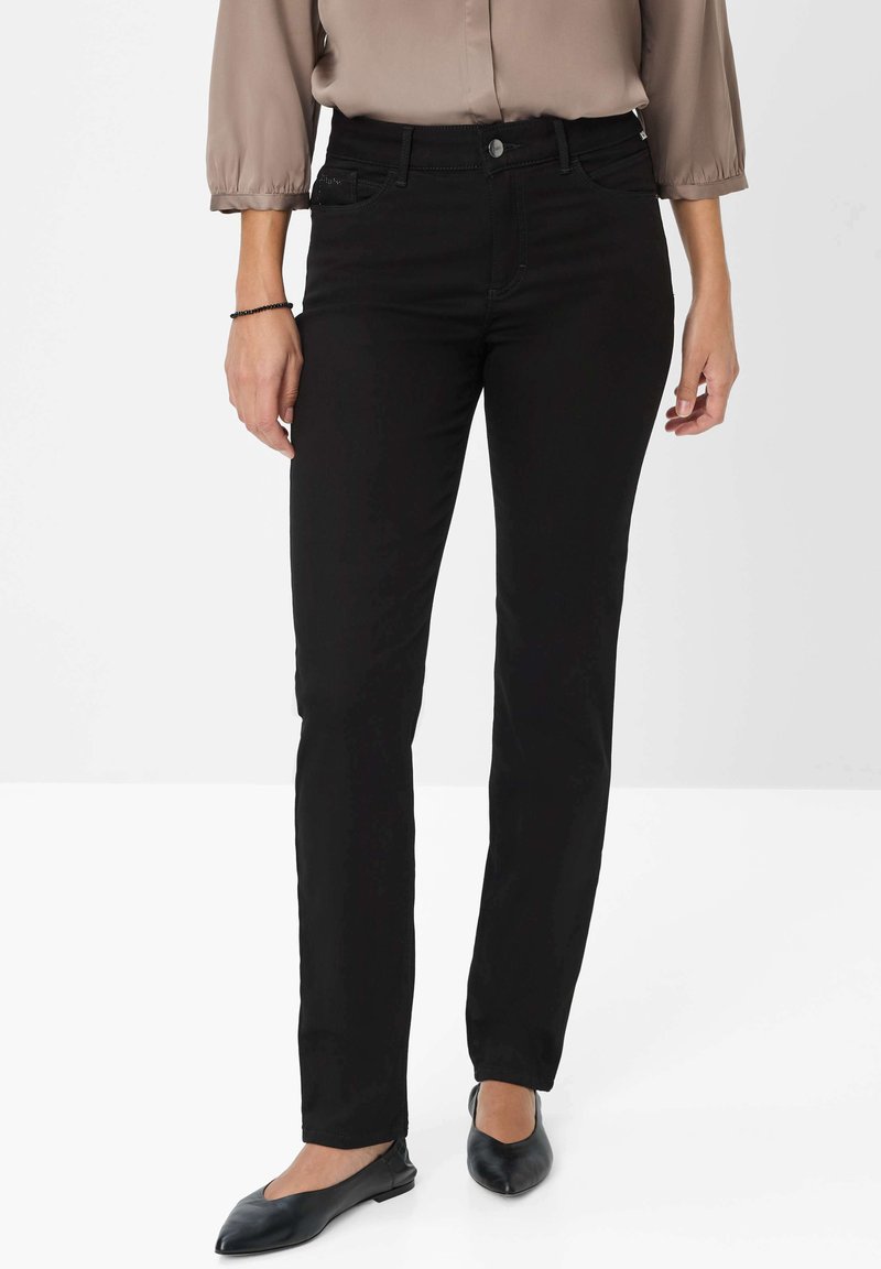 Jeans negros ajustados con una textura suave, corte recto y diseño de cinco bolsillos. Combinados con bailarinas negras y una blusa larga y ligera de manga larga.