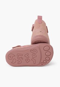 Scarpe in suede rosa con cinturino regolabile, suola testurizzata che presenta motivi embossati giocosi e una leggera lucentezza sul materiale superiore.