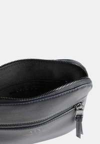 Borsa in pelle nera con chiusura a zip, esterno texturizzato, fodera interna liscia e logo in rilievo, con dettagli in metallo argentato.