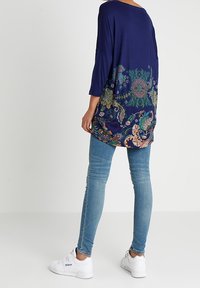 Tunique marine avec des motifs floraux colorés au bas, associée à un jean skinny bleu clair et des baskets blanches. Coupe décontractée et manches trois-quarts.