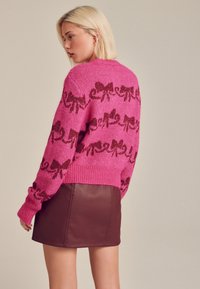 Stickad rosa tröja med kontrasterande bruna rosetter, rund halsringning och ribbade muddar. Matchad med en brun läderminikjol.