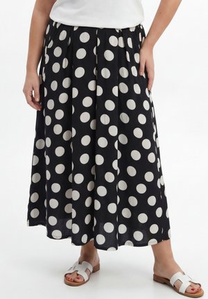 Black midi skirt with large white polka dots, paired with white slip-on sandals, shown from waist to feet.