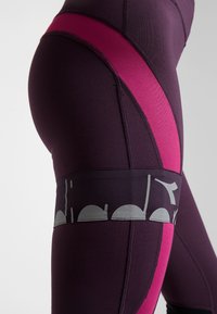 Leggings viola e rosa realizzati in un tessuto elastico e aderente. Presentano una banda grafica grigia e pannelli a contrasto per un design dinamico.
