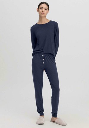 Navy Loungewear-Set mit langen Ärmeln, elastischem Bund und Knopfdetail. Weicher Stoff und eng anliegende Beine, kombiniert mit leichten Hausschuhen.