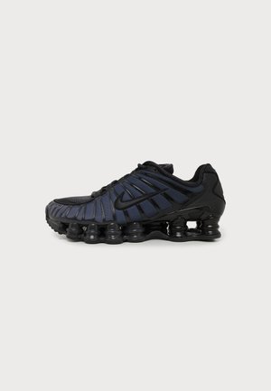 Baskets Nike noires et bleu marine avec semelle segmentée unique et dessus en mesh, vues de profil sur un fond uni.