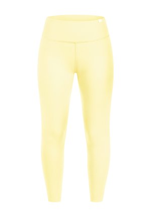 Close-up af en persons talje iført bleggule leggings med høj talje med synlige syninger og en lille stofetiket ved linningen.