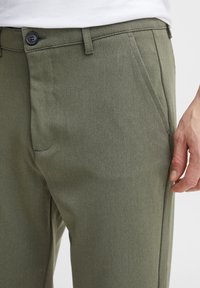 Olive green trousers made from textured fabric, featuring side pockets and a front button closure, with tailored fit for a clean silhouette.
