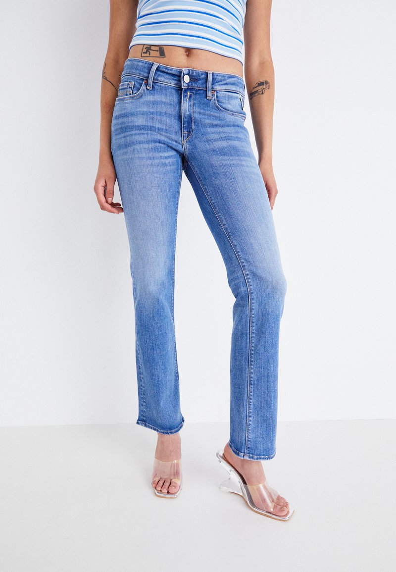 Jeans de mezclilla azul claro con diseño de pierna recta, que cuentan con cinco bolsillos y un cierre de boton. Llevados con sandalias de tacón transparente.