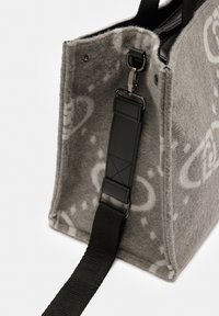 Borsa grigia in feltro con motivi paisley bianchi, dotata di una tracolla nera staccabile con attacchi in pelle e metallo.