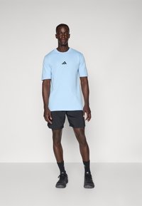 T-shirt de manga curta azul claro com um logótipo preto no peito, combinado com calções de desporto pretos e ténis pretos.