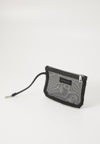 Svart nätpåse med dragkedjestängning, med ett dekorativt handtag och en logotag. Designen är rektangulär med en genomskinlig textur.