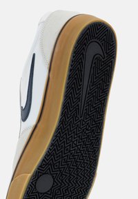 Vita och beige sneaker med gummisula med ett svart fiskbensmönster, en svart Swoosh-logotyp och texturerade mockadetaljer.