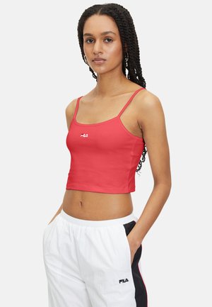 Röd kort tanktop med tunna axelremmar, prydd med en vit Fila-logotyp på bröstet. Modellen bär vita byxor med svarta och röda accenter.