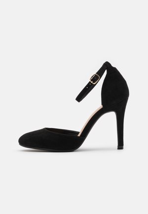 Black suede high-heeled pump with a rounded toe, ankle strap featuring a gold buckle, and a sleek, curved silhouette.