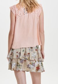 Blusa rosa claro con mangas de encaje y una falda de volantes beige con estampados de flores coloridas. Tejido suave y fluido.