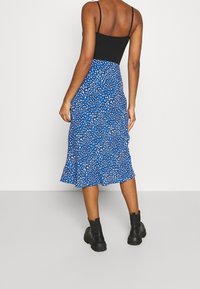 Blauwe bloemen midi-skirt met een gerimpelde zoom, gemaakt van lichte stof, featuring een verspreid patroon van wit en lichtblauw. Draagt met zwarte enkellaarsjes.