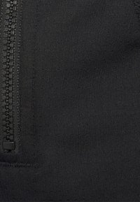 Svart zip-up tyg med strukturerat rippat mönster, med detaljer av svart dragkedja längs sidan. Materialet verkar vara elastiskt och slätt.