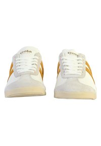 Baskets blanches avec suède gris et accents orange, featuring un laçage à l'avant, une semelle en caoutchouc et un logo sur la languette. Design simple.