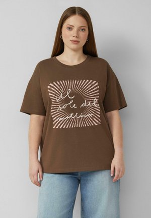 Jonge vrouw met stijl bruin haar draagt een bruin oversized T-shirt met roze zonnestralen en Italiaanse tekst, gecombineerd met lichtblauwe spijkerbroek.
