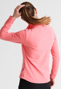 Różowy polarowy sweter z długim rękawem i wysokim kołnierzem. Posiada płaskie szwy i boczną metkę. Miękka tekstura, regularny krój.