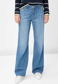 Jeans azzurri a gamba larga realizzati in denim, con chiusura a bottone, passanti per cintura e cuciture a contrasto. Abbinati a sneakers bianche.