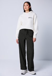 Bluza w kolorze off-white z kapturem i czarnym nadrukowanym tekstem; zestawiona z ciemnoszarymi spodniami w prążki z regulowanym paskiem.