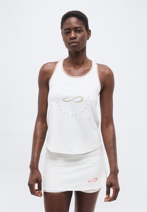 Atletische vrouw die een witte mouwloze top en bijpassende rok met oneindigheidslogo's draagt, staand tegen een effen lichte achtergrond.