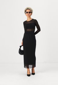 Juodas suknelė su permatomu tinkleliu viršuje ir tvirtu sijonu. Papuošta juoda rankine ir smailiomis aukštakulnėmis bateliais. Įtrauktos saulės akinių.