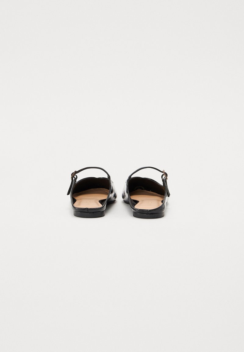 Chaussures en cuir verni noir avec un dos ouvert et une fine lanière. Présentent une texture lisse et un design minimaliste. Semelle plate.