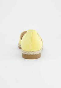 Geel suède espadrille-achtige schoen met een zool van gevlochten jute en een tankleurige rubberen buitenzool, met een afgeronde achterkant en minimale details.