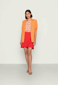 Blazer laranja, blusa floral, saia vermelha com babados e sandálias laranja. Texturas suaves, cores vibrantes e detalhes de design em camadas.