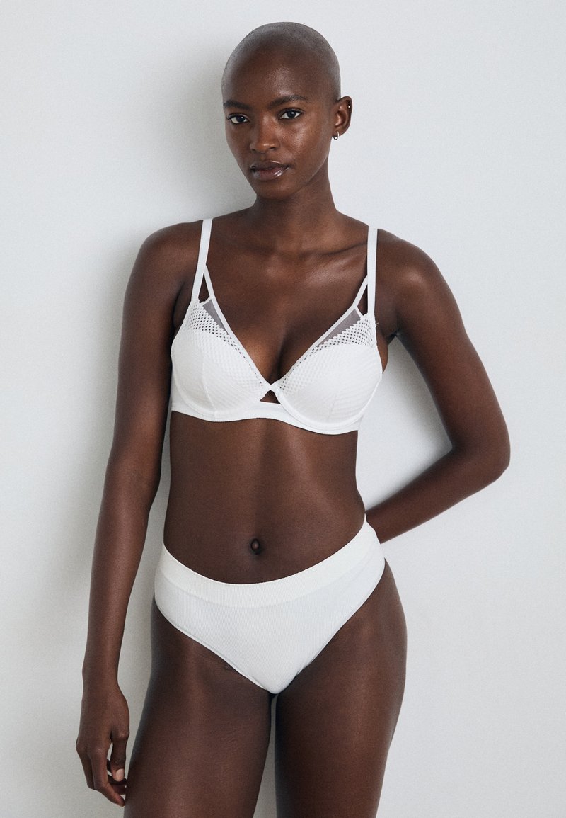 Hvit lingerisett med en teksturert bh med trekantkopper og justerbare stropper, kombinert med høytlivet, ribbet bikiniunderdeler.