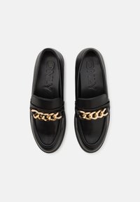 Paire de mocassins en cuir noir avec détail de chaîne dorée sur le dessus et nom de la marque "ONLY" embossé sur les semelles intérieures.