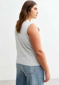 Grijze mouwloze trui van een zachte brei, met een ronde halslijn en geribbelde zoom, gedragen met lichtblauwe high-waisted jeans.