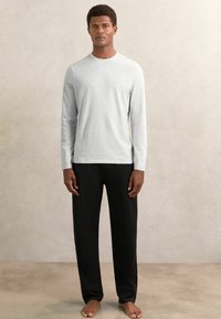 Dlhý rukáv svetlosivého trička z jemného materiálu v kombinácii s voľnými čiernymi nohavicami. Minimalistický dizajn bez viditeľných vzorov.