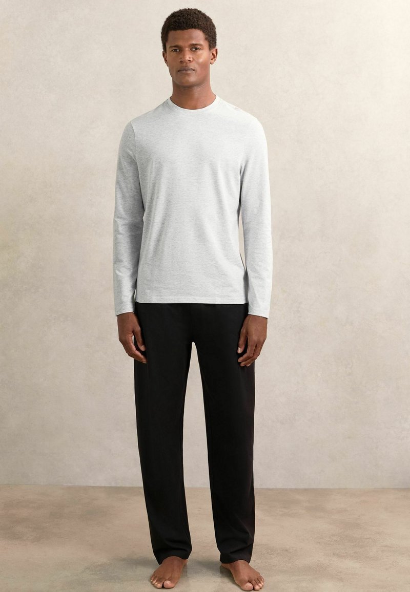 Dlhý rukáv svetlosivého trička z jemného materiálu v kombinácii s voľnými čiernymi nohavicami. Minimalistický dizajn bez viditeľných vzorov.