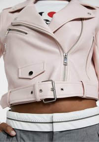 Rosa Kunstleder Motorradjacke im Cropped-Stil mit silbernen Reißverschlüssen, Druckknopf-Beschlägen, vorderer Tasche und tailliertem Bund. Gestylt mit einem grauen Bund.