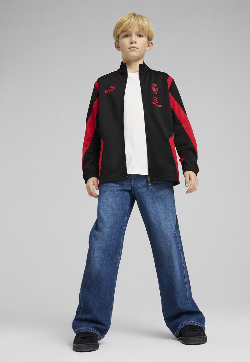 Sort og rød lynlåsjakke med logo, parret med lys blå jeans og sorte sko. Outfittet har en afslappet sportstil.