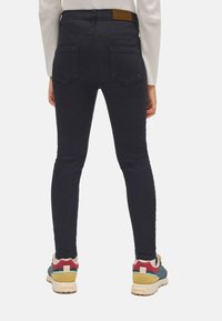 Vaqueros ajustados de color azul oscuro de mezclilla, con dos bolsillos traseros y una etiqueta de cuero en la cinturilla, combinados con zapatillas coloridas.