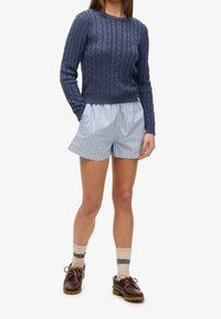 Pull en tricot à torsades bleu marine, short rayé bleu clair, chaussettes crème avec accents bleus, chaussures bateau marron à lacets et semelles en caoutchouc.