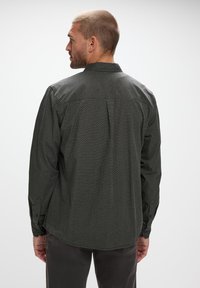 Camisa de botones verde oscuro con un patrón geométrico, mangas largas, cuello y detalle de pliegue en la espalda. Tela texturizada y corte entallado.