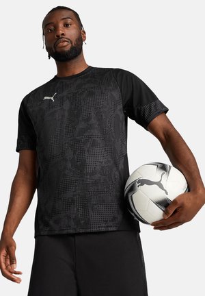 Zwart sportshirt met korte mouwen en een textuurpatroon, met het Puma-logo. Model houdt een zwart-wit voetbal vast en draagt zwarte shorts.