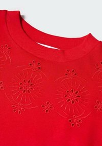 Pull rouge à col rond avec des motifs floraux découpés et brodés sur la poitrine, disposés de manière symétrique.